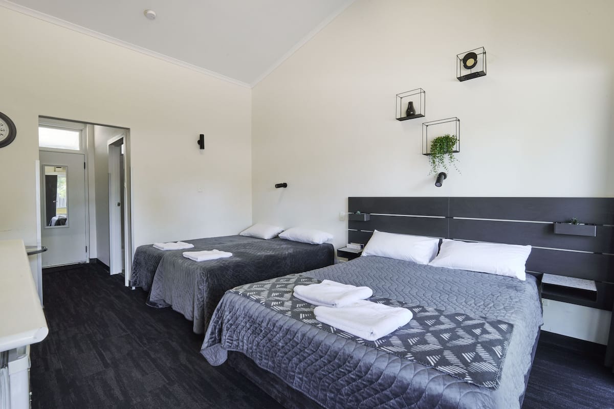 A hotel room with two beds, a dark wood floor, a white door, and a small plant on the wall.