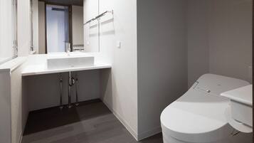 Un baño moderno con lavamanos, inodoro y zona de ducha blancos.