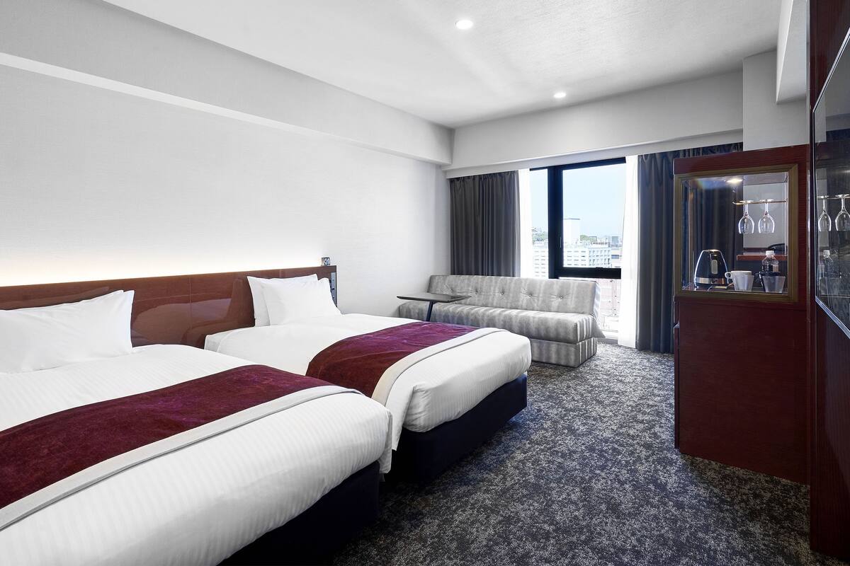 Habitación de hotel con dos camas, un sofá, una mesita y un minibar.