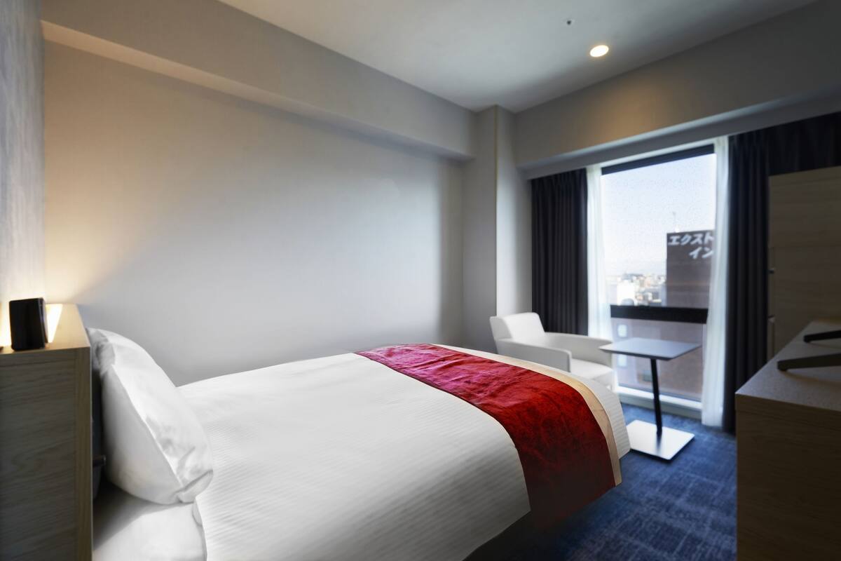 Habitación de hotel con cama, escritorio, silla y vista a la ciudad por la ventana.