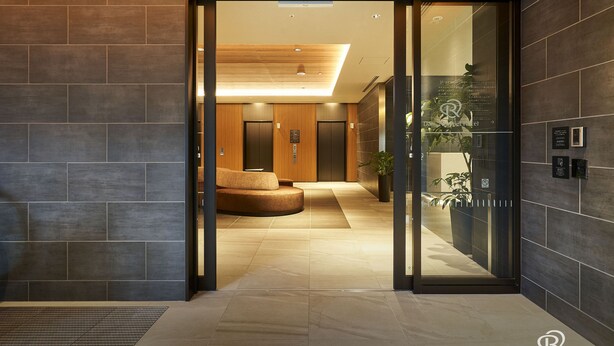 A modern hotel lobby with a curved seating area, a reception desk, and a glass partition.