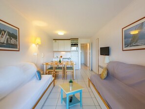 Un espacio habitable compacto con dos sofás, una mesa de comedor, una zona de cocina y un televisor.