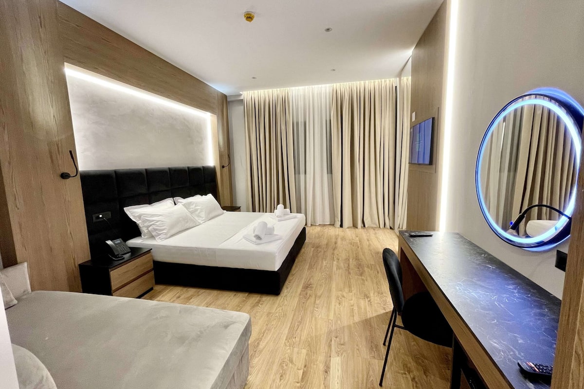Une chambre d’hôtel comprenant un lit, une table de chevet, une chaise et un miroir rond avec éclairage.