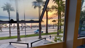 A view from a window overlooking a beach with palm trees and a sunset. - EL MAR HOTEL (Vlorë)