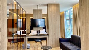 A modern hotel room with a large flat-screen TV, a sofa, a dining area with a table and chairs, and a large window with curtains. - EL MAR HOTEL (Vlorë)