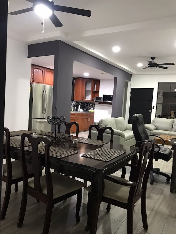 A modern living room with a dining area, a kitchen, and a ceiling fan.