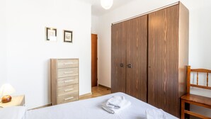 Ein Schlafzimmer mit einem Bett, einem Holzschrank, einer Holzkommode und einem Holzsessel.