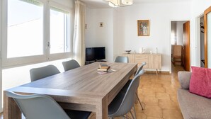 Ein geräumiger Essbereich mit einem langen Holztisch, mehreren Stühlen, einem Fernseher und einer kleinen Vitrine mit Dekoration.