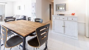 Un comedor con una mesa y sillas de madera, un armario blanco con cajones y un espejo sobre el armario.