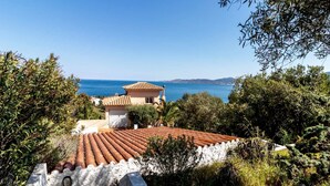 En villa vid kusten med tak belagt med terrakottafärgade tegelpannor, ett litet torn och utsikt över havet.