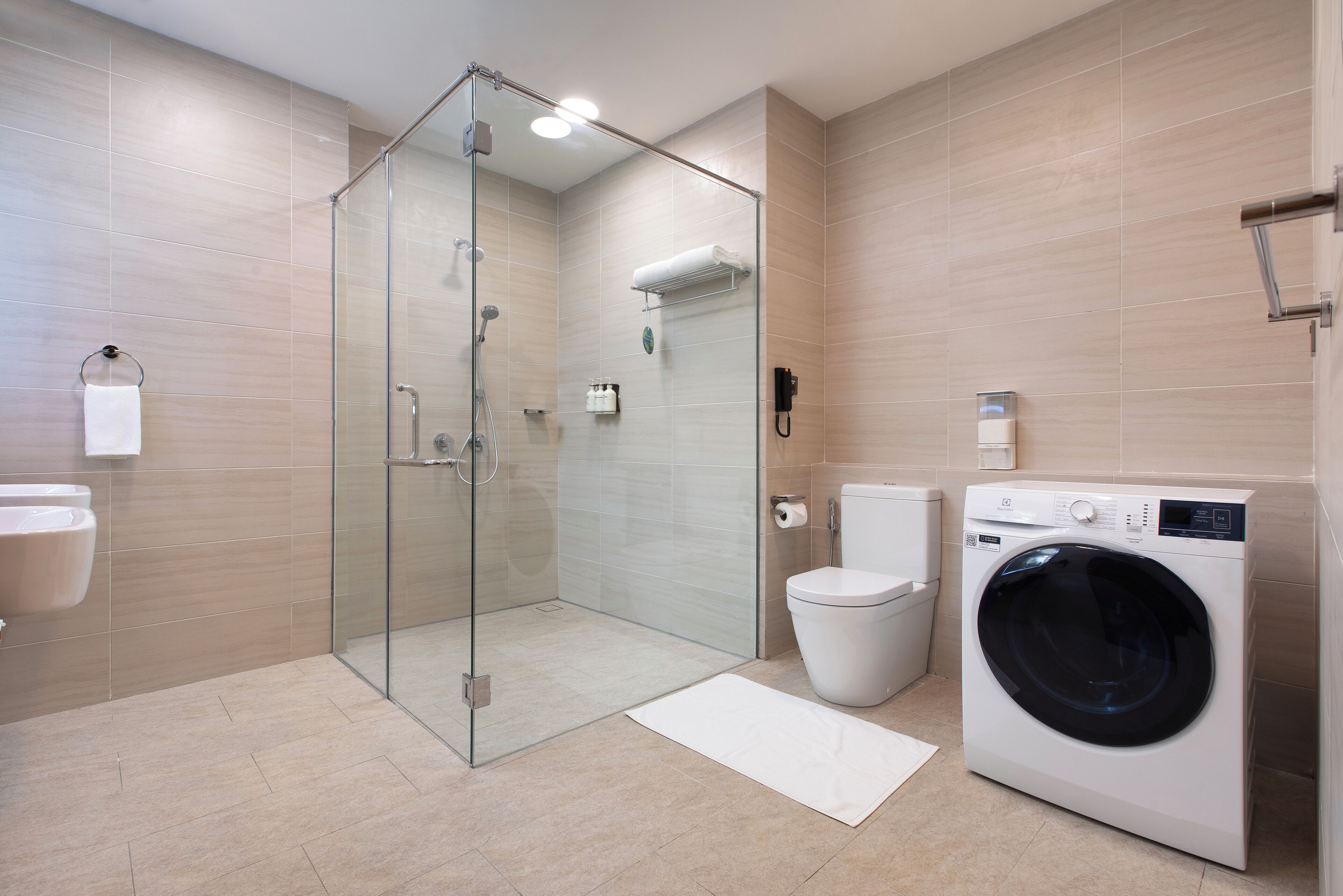 A modern bathroom with a glass-enclosed shower, a toilet, a washing machine, and a sink.