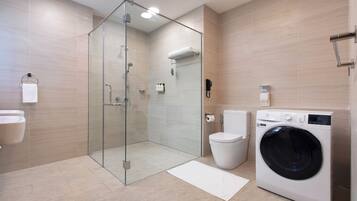 A modern bathroom with a glass-enclosed shower, a toilet, a washing machine, and a sink.