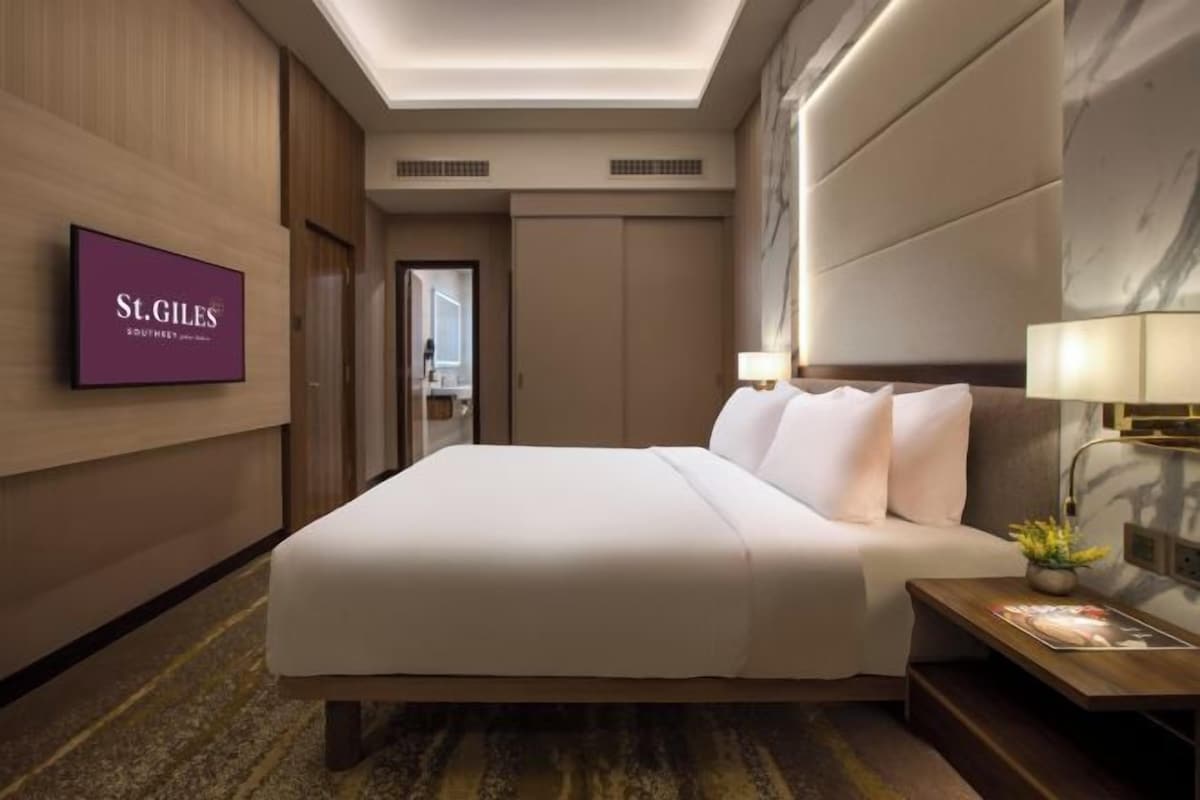 A hotel room with a large bed, a TV mounted on the wall, and a nightstand with a lamp.