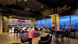 A modern bar area with a city view, featuring a bar counter, seating, and a decorative light fixture. - St. Giles Southkey (Johor Bahru)