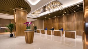 A modern hotel lobby with a reception desk, wooden paneling, and a decorative chandelier. - St. Giles Southkey (Johor Bahru)