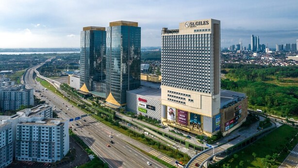 A modern hotel with a prominent St. Giles sign, two tall glass buildings, and a busy highway in the background.