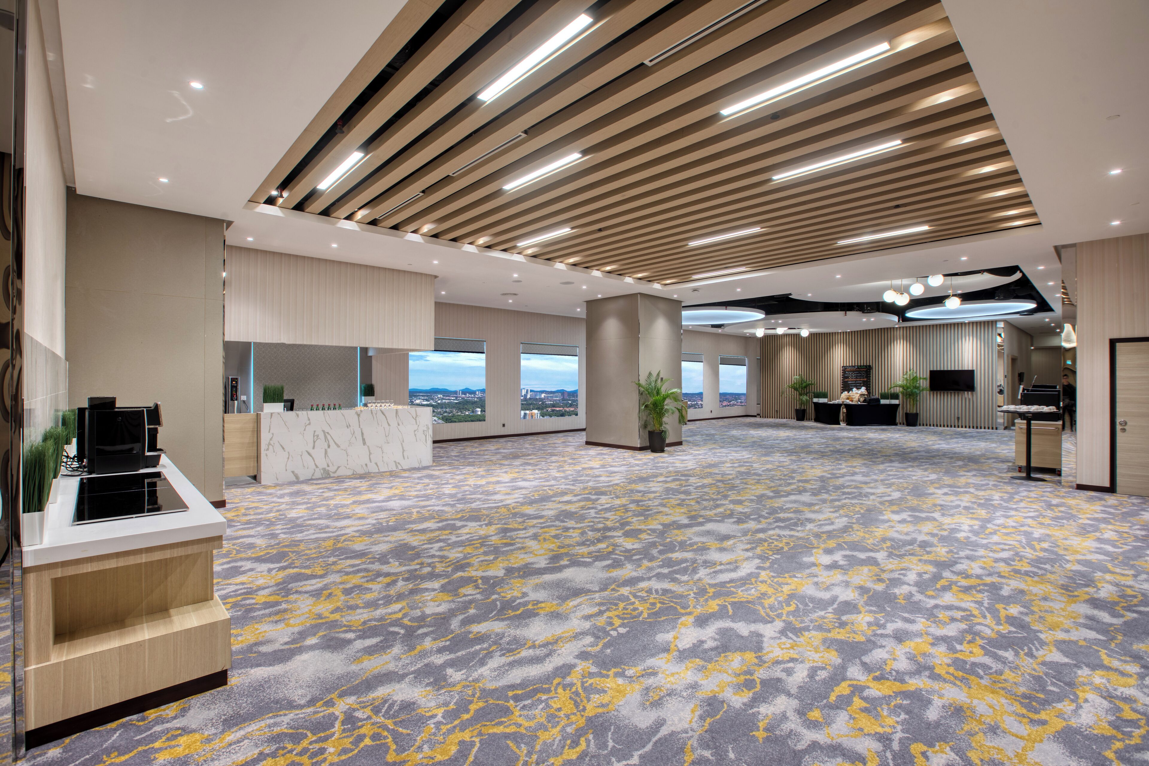 A spacious hotel lobby with a modern design, featuring a reception desk, seating area, and large windows offering city views.