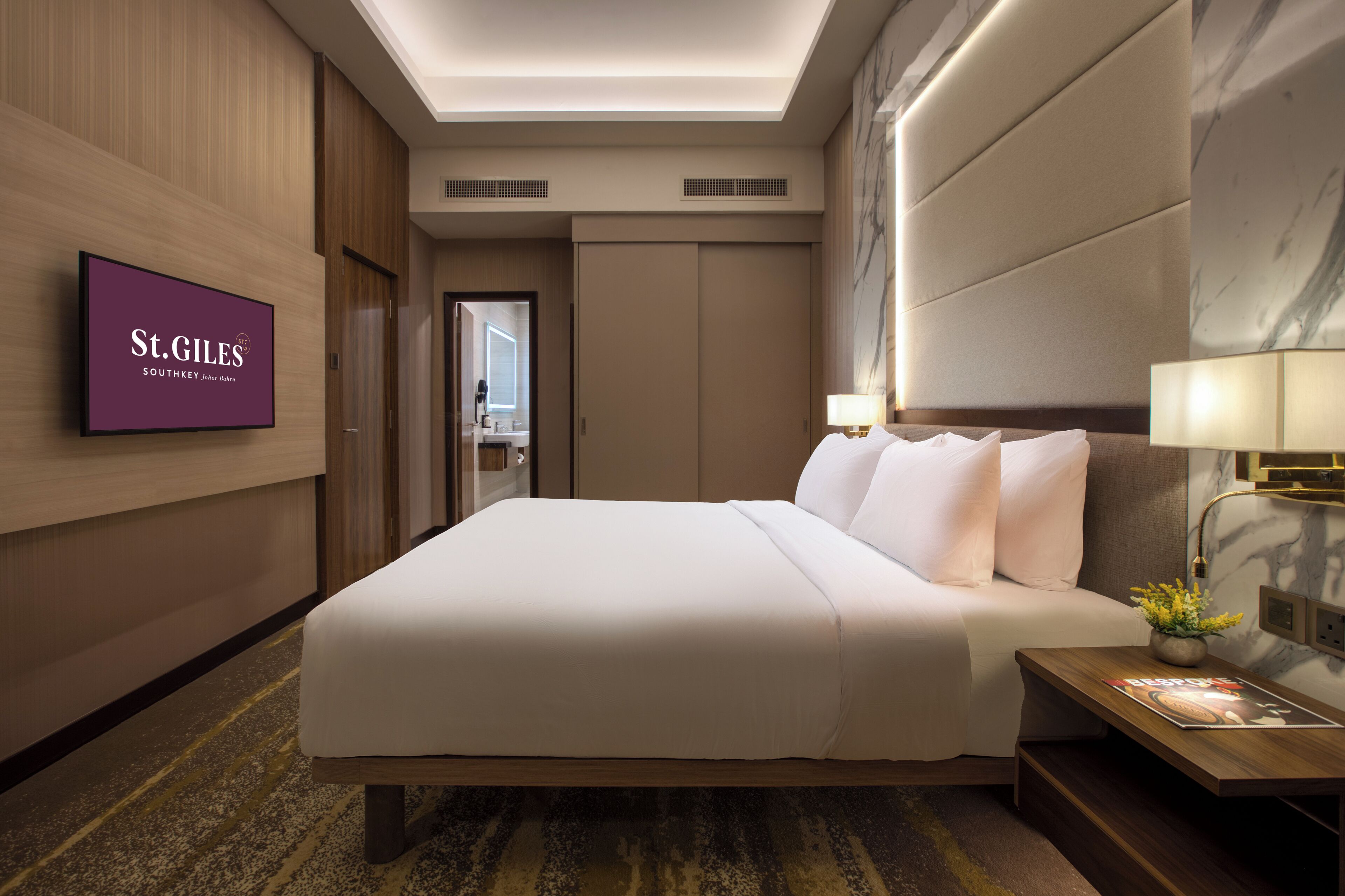 A hotel room with a large bed, a TV mounted on the wall, and a nightstand with a lamp.