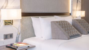A neatly made bed with white linens and patterned pillows, a bedside table with a book, and a wall-mounted lamp.
