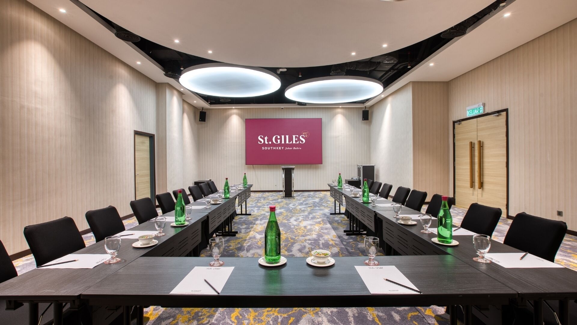 A conference room with a long table, chairs, and a large screen displaying "St. GILES SOUTHKEY Johor Bahru".