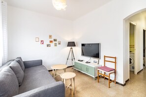 Ein Wohnzimmer mit grauem Sofa, Fernseher, Schreibtisch, Lampe und Sessel.