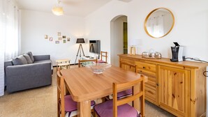 Una habitación acogedora con una mesa de madera, un sofá gris, un televisor, una lámpara y una máquina de café.