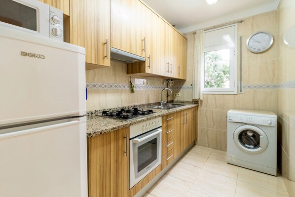 A compact kitchen with wooden cabinets, a built-in oven, a gas stove, a sink, and a washing machine.