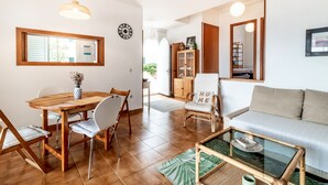 Una sala de estar con un sofá, una mesa de comedor con sillas, una mesa de centro de vidrio y una estantería.