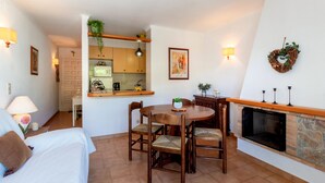 A cozy room with a dining table, chairs, a fireplace, and a kitchen area with a microwave and a hanging plant. - Sant Carles 24 - apartment with terrace (Llança)