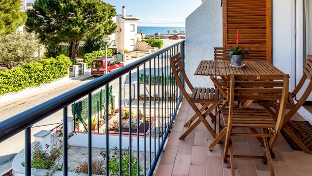 A balcony with a wooden table and chairs, a potted plant, and a view of the street and buildings. - Sant Carles 24 - apartment with terrace (Llança)