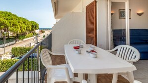 A balcony with a white table and chairs, a view of the street and trees, and a door with wooden shutters. - Sant Carles 25 - apartment with terrace (Llança)