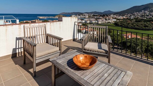 A balcony with two wooden chairs and a table, overlooking a coastal town and mountains. - Sant Genís 19 - top-floor apartment with terrace (Llança)