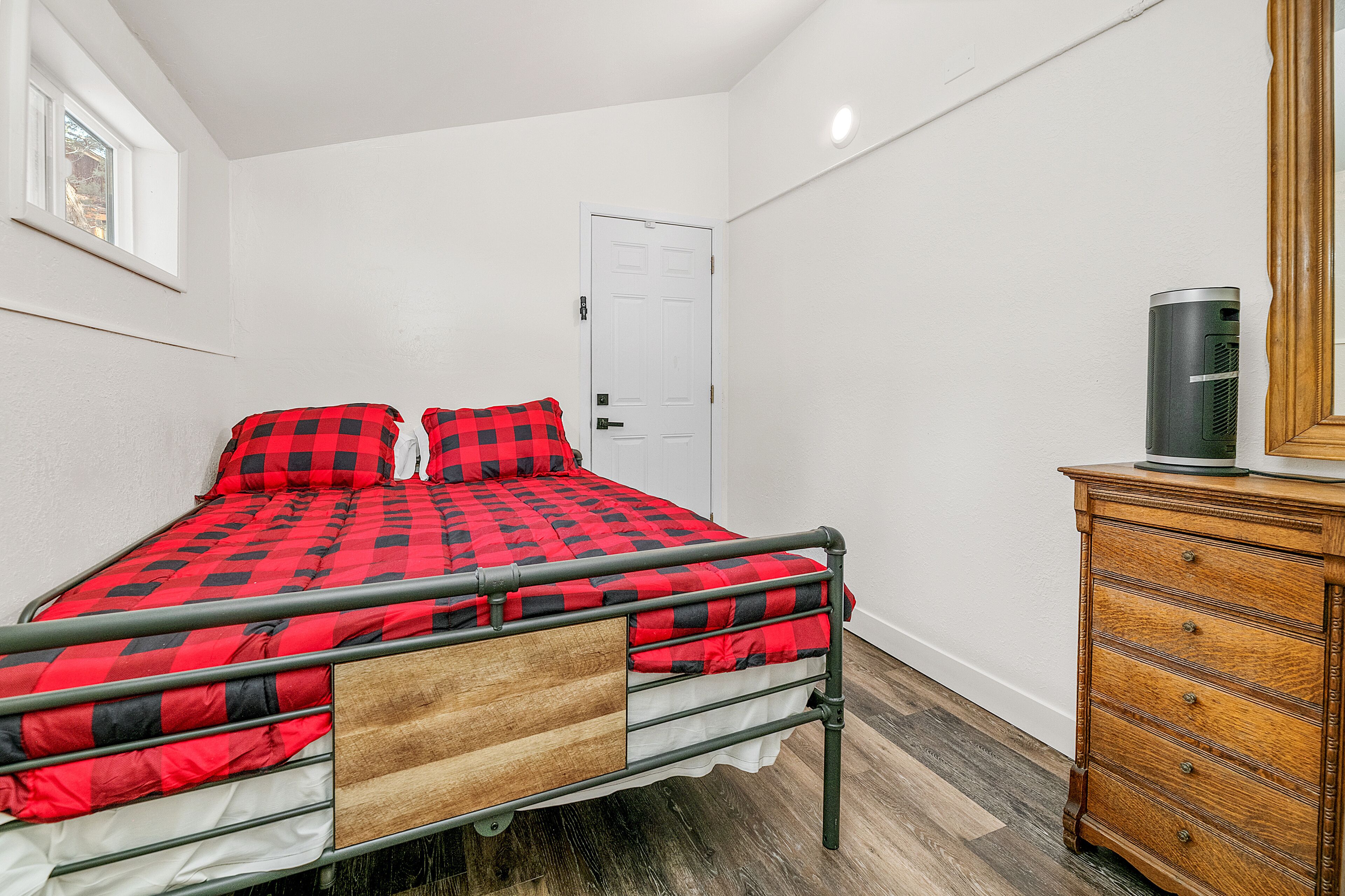 A bedroom with a metal bed frame, a wooden dresser, and a white door.