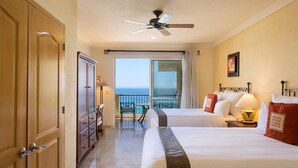 A hotel room with two beds, a balcony with a view of the ocean, a ceiling fan, and a desk with a lamp. - Luxury resort on the beach - walking to downtown (Cabo San Lucas)