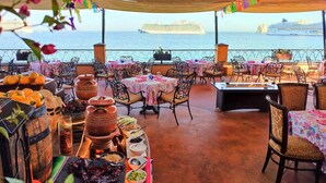An outdoor dining area with tables and chairs, a view of the sea, and a cruise ship in the background. - Luxury resort on the beach - walking to downtown (Cabo San Lucas)