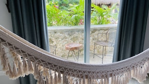 A hammock in a room with a view of a garden and a thatched-roof structure. - Jaakbal Tulum (Tulum)