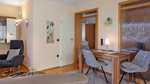A modern living room with a wooden dining table, two grey armchairs, a sofa, and a fireplace. - Apartment 'Fuldatalblick' with Garden & Wi-Fi (Fulda)