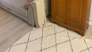 Ett vardagsrum med en soffa, ett träskåp med glasdörrar, en inramad tavla på väggen och en mönstrad matta.