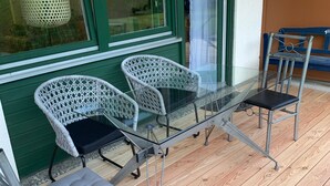 Ett takförsett utomhusområde med sittplatser, bestående av metallstolar och ett bord i glas.