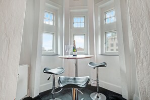 A corner room with a round table, two bar stools, and a bottle of champagne.
