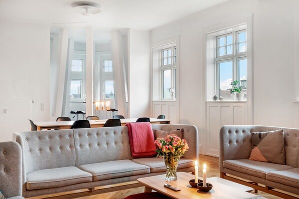 Una sala de estar moderna con un sofá gris, una mesa de centro con un jarrón de flores y una zona de comedor con una mesa y sillas.
