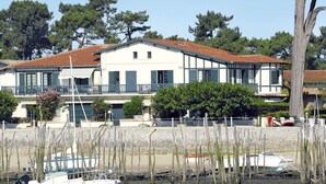 A waterfront property with a large building featuring a balcony, a boat docked nearby, and a clear view of the water. - Cosy apartment for 4 people with TV, terrace and pets allowed (Bélisaire)