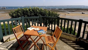 A wooden table and two chairs on a balcony overlooking a beach with boats and a distant shoreline. - Cosy apartment for 4 people with TV, terrace and pets allowed (Bélisaire)