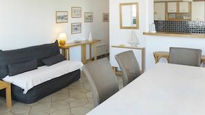 A room with a sofa, a dining table, chairs, a lamp, a small table with a lamp, and a kitchen area with cabinets and a mirror. - Cosy apartment for 4 people with TV, terrace and pets allowed (Bélisaire)