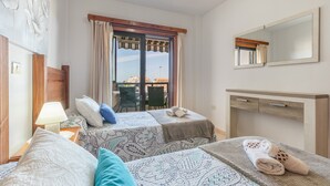 Camera d'albergo con due letti, una scrivania, una sedia, una finestra con tende e vista sugli edifici.