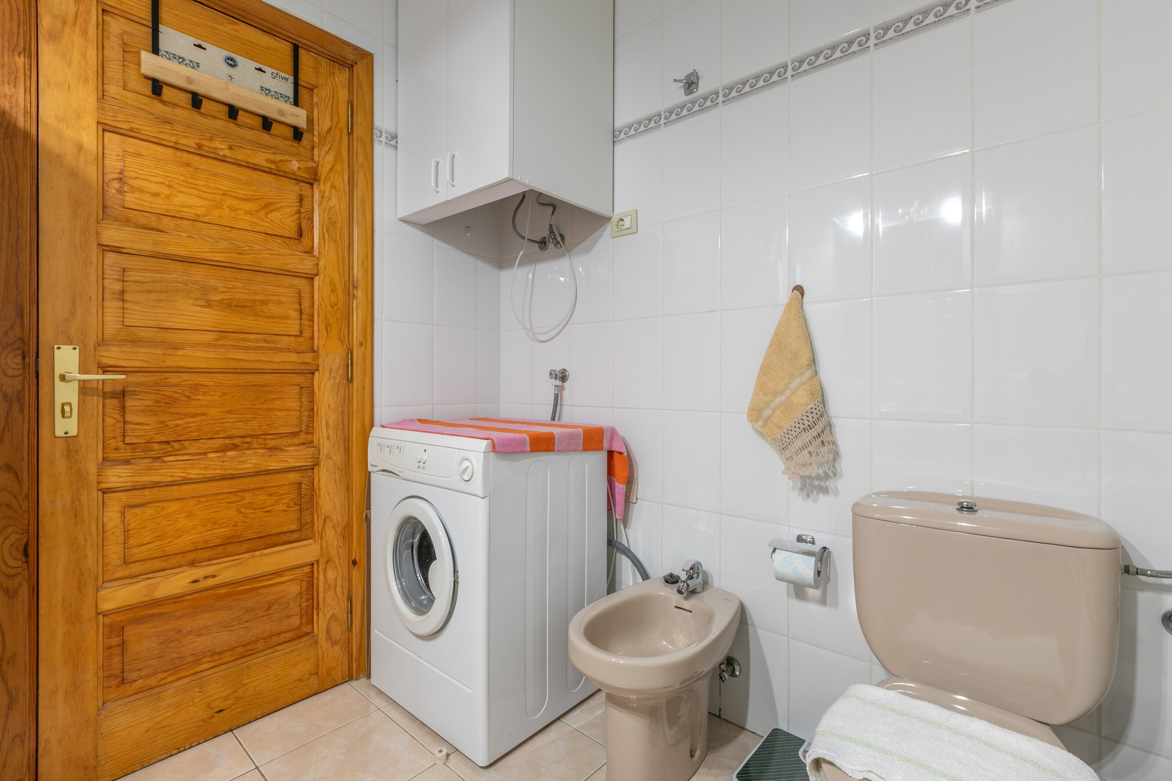 A compact bathroom with a wooden door, a washing machine, a bidet, and a toilet.