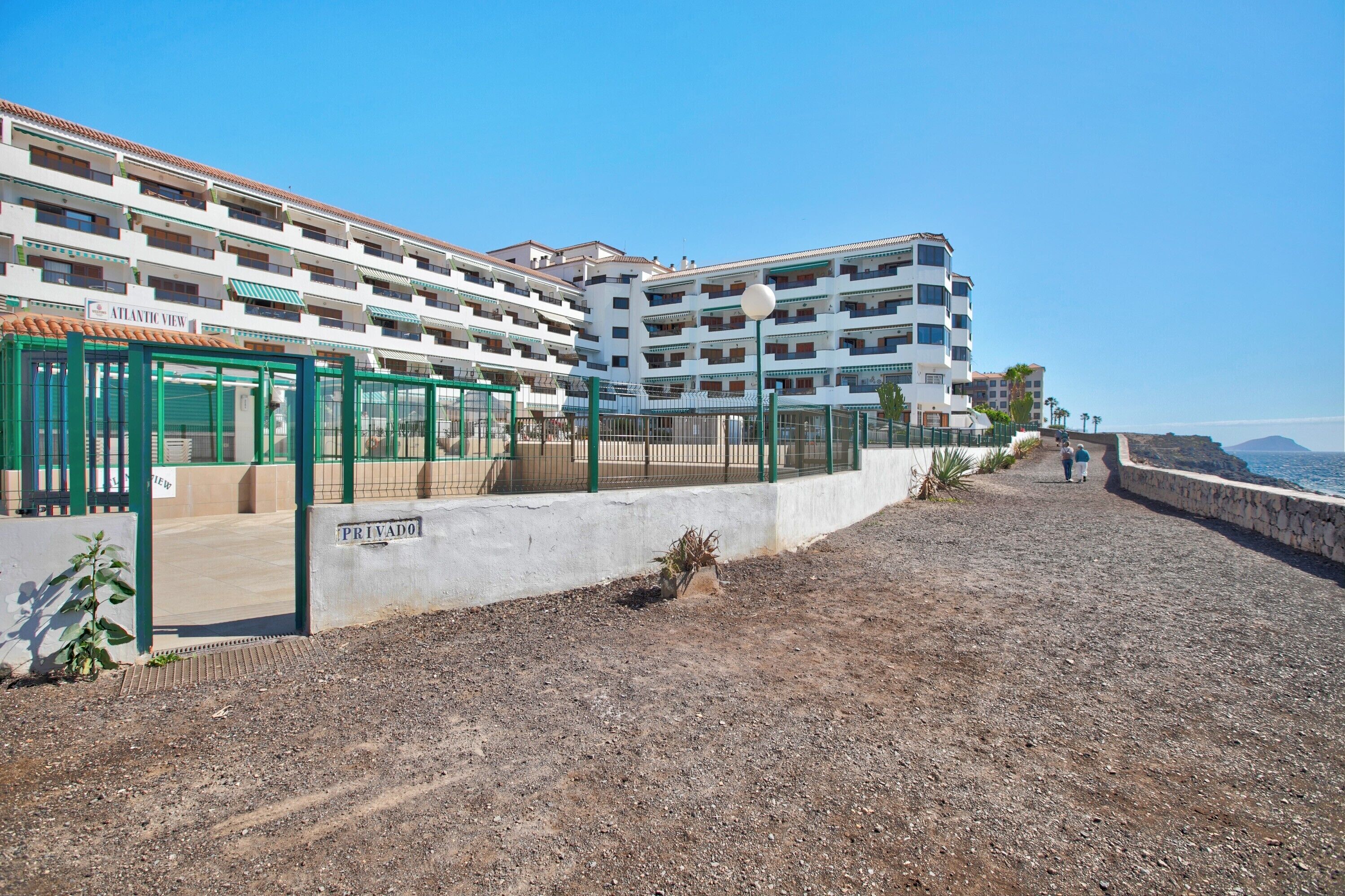 A multi-story hotel with balconies, a covered walkway, and a view of the sea.