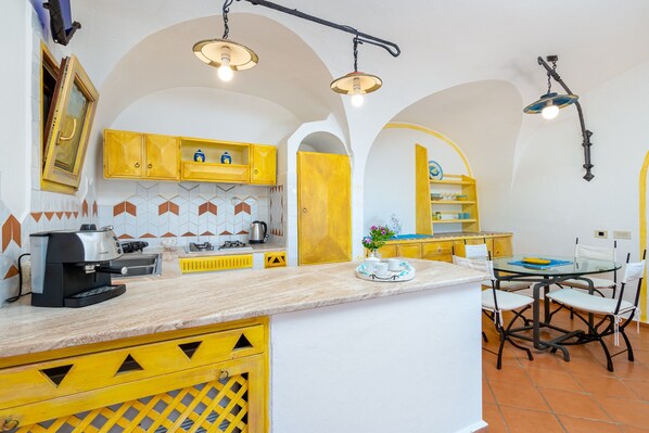 Una cocina con armarios amarillos, una cafetera y un comedor con mesa y sillas.