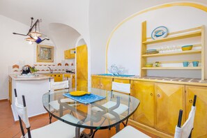 Une cuisine moderne avec une table à manger en verre, des meubles de rangement jaunes et une étagère décorative.