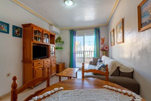 Una sala de estar con un mueble bajo de madera para el televisor, un sofá, una mesa de comedor y un balcón con vistas.
